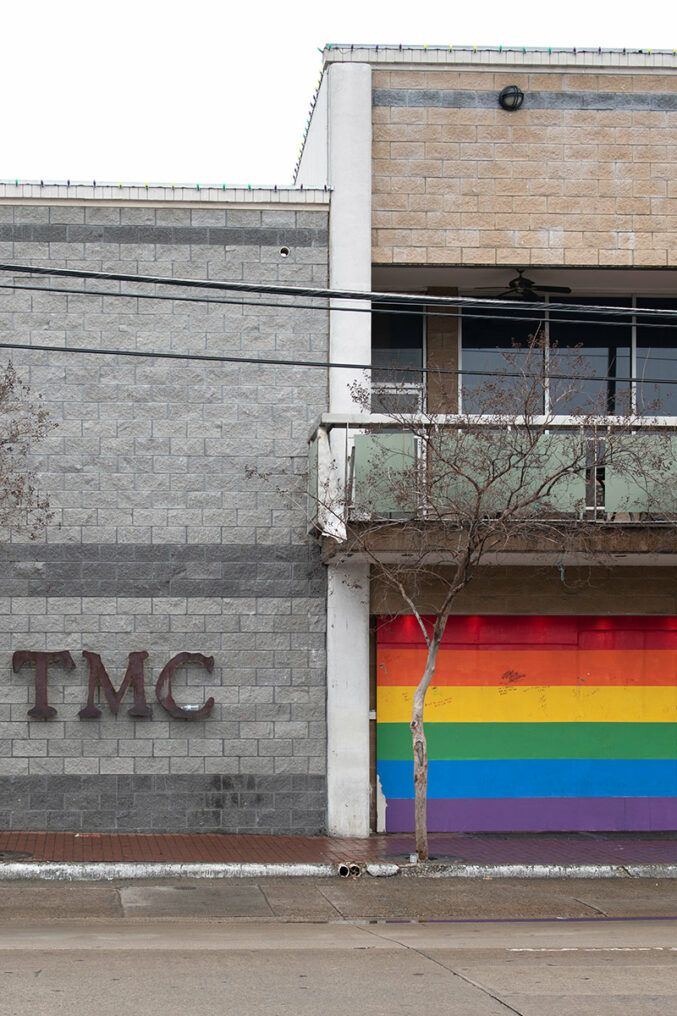 The TMC venue today — a gray brick building with a large red TMC sign and a rainbow-painted garage door, on Cedar Springs Road in Dallas.